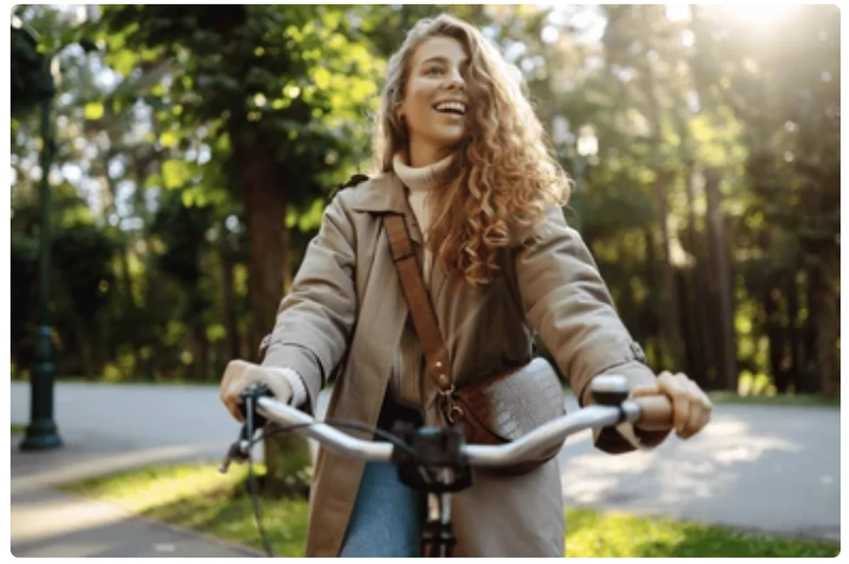 Smiling woman riding a bicycle through a sunny green park