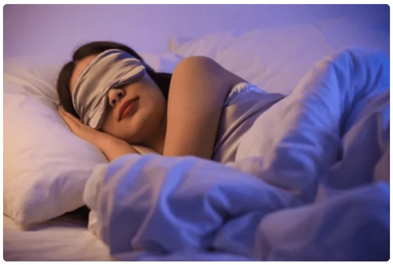 Woman wearing a soft sleep mask resting peacefully in bed under calming blue evening light