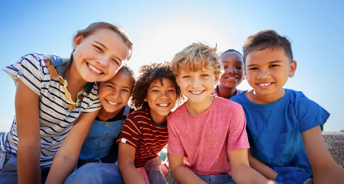 Group of happy children smiling together outdoors in bright sunlight